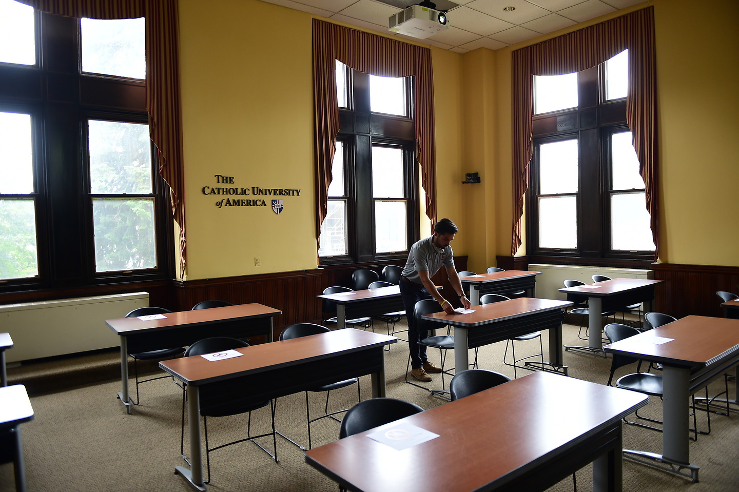 An empty classroom inside McMahon Hall. A maintenance worker adjusts one of the desks.